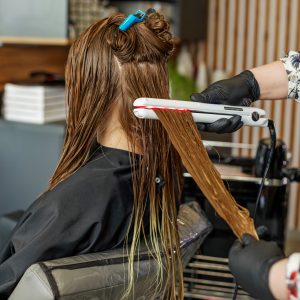 Professional hairdresser straightening long hair using straightener. Hair keratin.